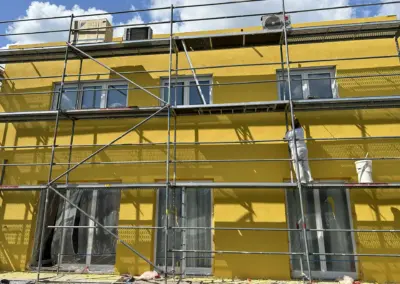 Kräftiger gelber Fassadenanstrich an einem Mehrfamilienhaus mit Gerüst
